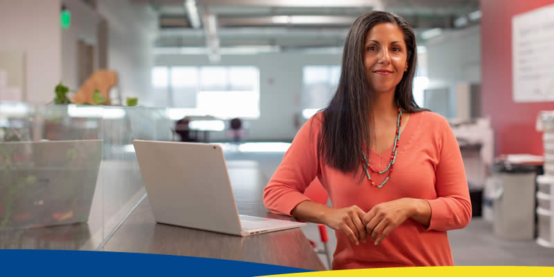 Mulher, usando camisa rosa, apoiada em balcão ao lado de um notebook
