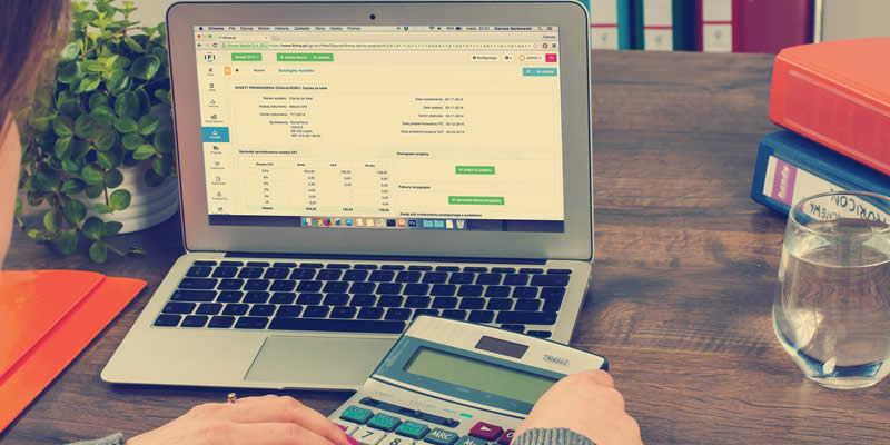 Mulher realizando operações financeiras em frente ao computador, com uma calculadora em mãos